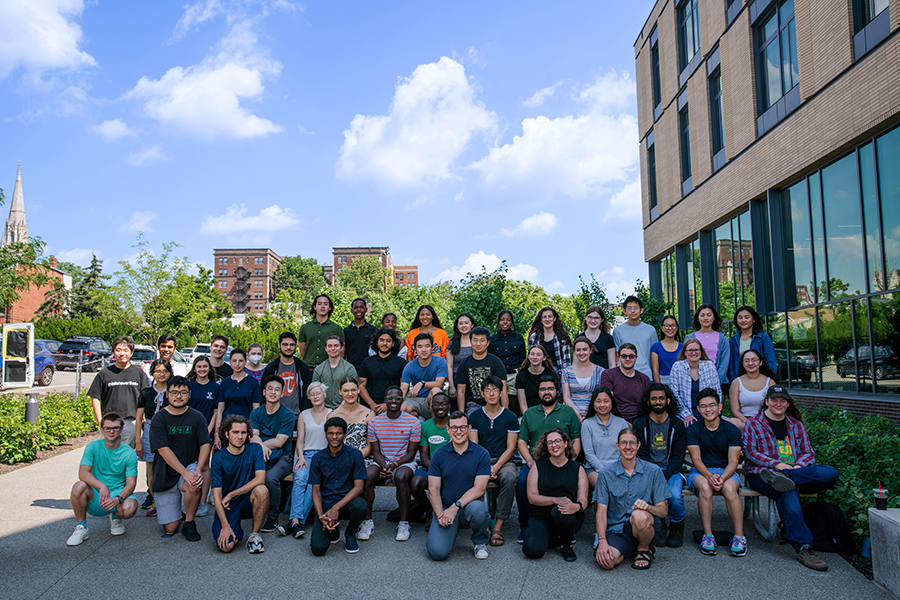  A group shot of students in front of college buildings on a sunny summer day.