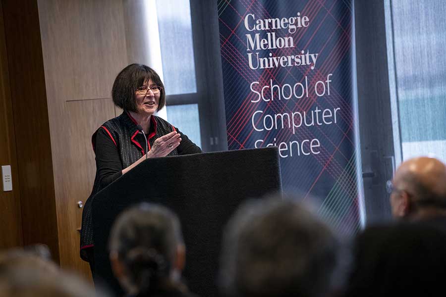  A woman with dark hair stands at a podium in with a banner to her side that reads Carnegie Mellon University School of Computer Science.
