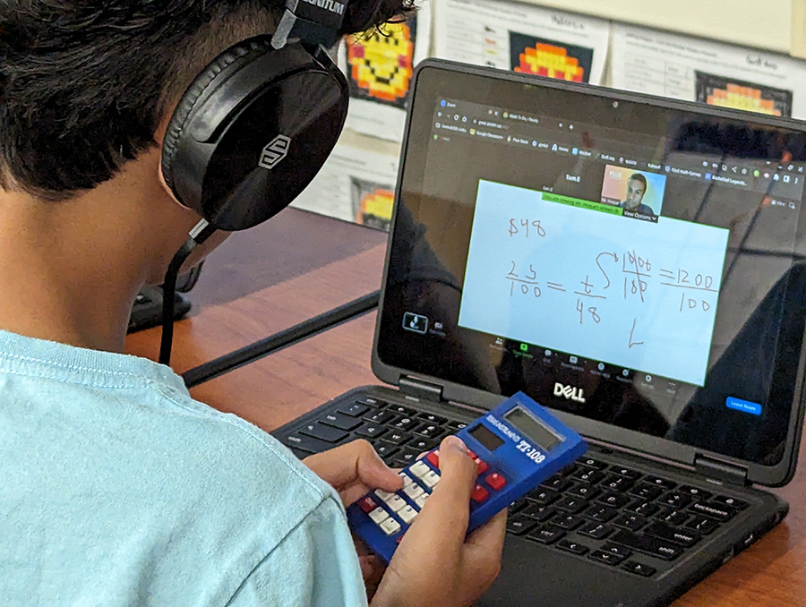  A student wearing headphones works on a laptop, the screen of which shows a math problem and a human tutor in a small box in the corner.