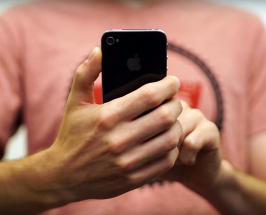  A person in a pink shirt holds an smart phone with one hand while tapping on the screen with another.