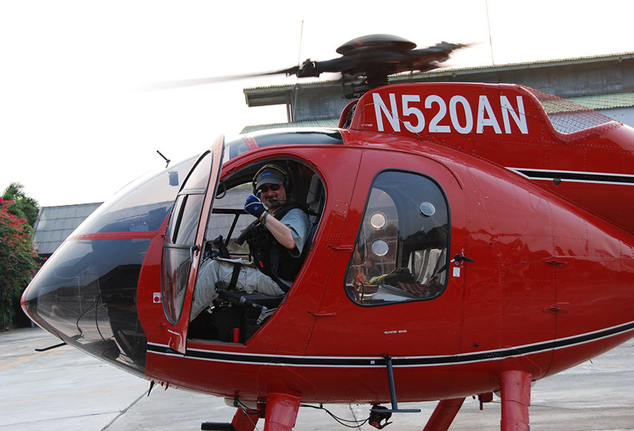  A man in sunglasses sits in a red helocopter giving a thumbs-up signal.